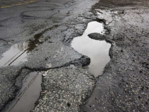 Badly damaged asphalt road with rain-filled potholes